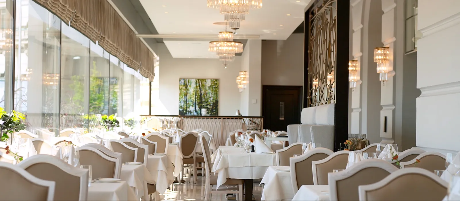 The Veranda dining room: white-clothed tables and pale chairs along the glass front, under small crystal chandeliers.