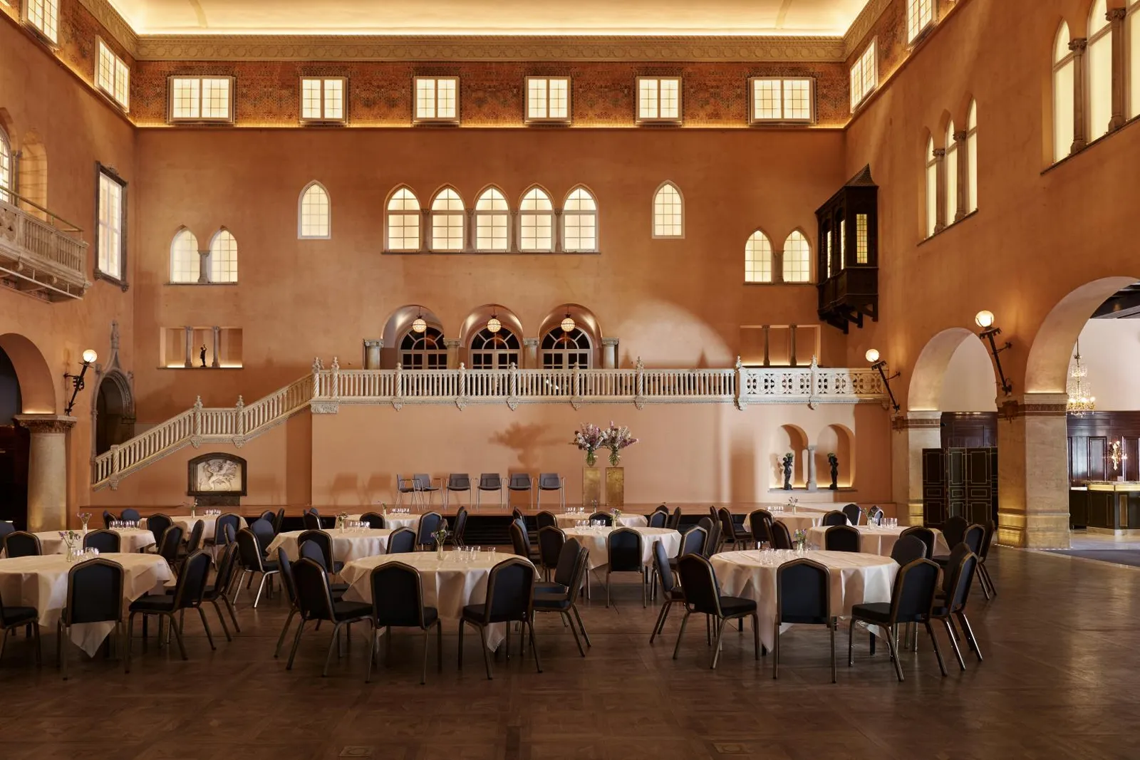 The Vinterträdgården laid with round tables: a hall as tall as a courtyard, with terracotta walls, rows of arched windows and a white gallery.