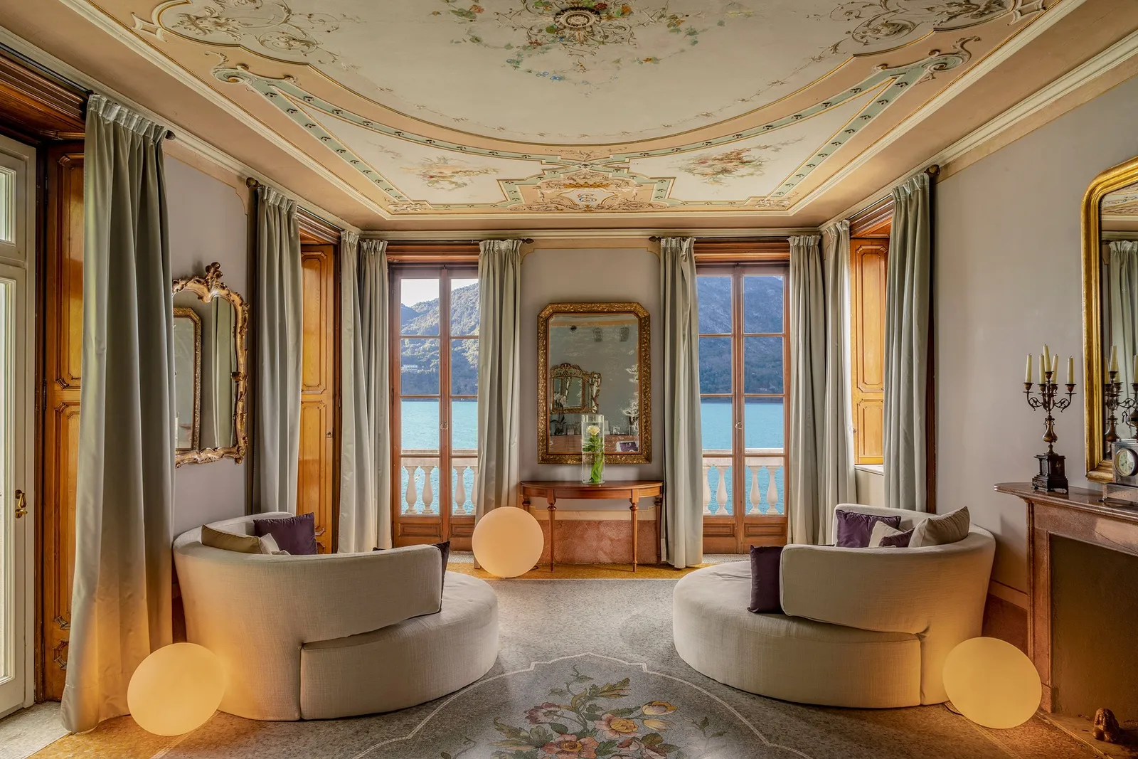 Il salone affrescato della T Spa in Villa Emilia, con due poltrone chiare e le porte-finestre sul lago