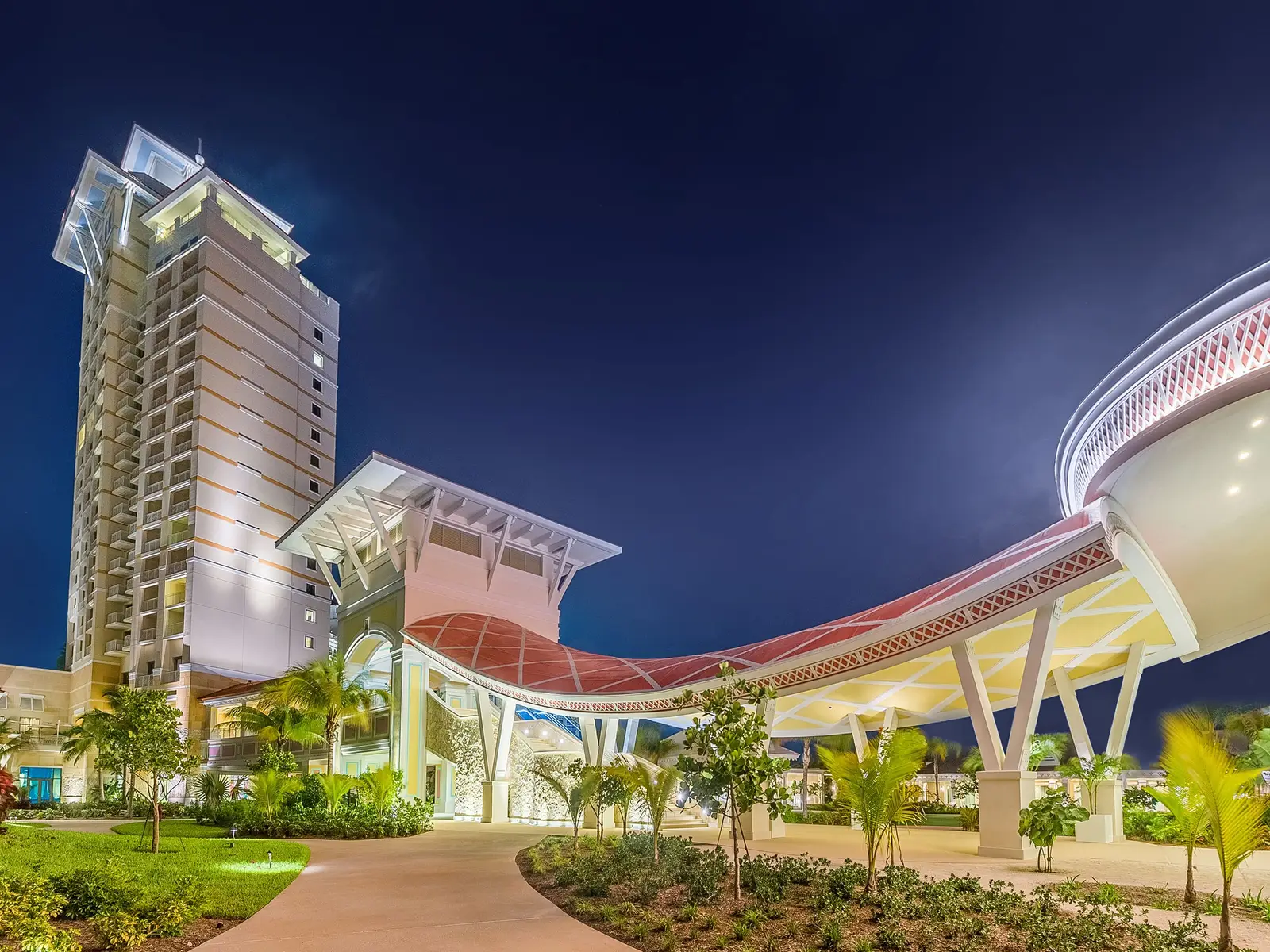 At dusk, the curved canopy of the Baha Mar Convention, Arts & Entertainment Center, its pierced ceiling lit, with one of the resort’s towers behind.