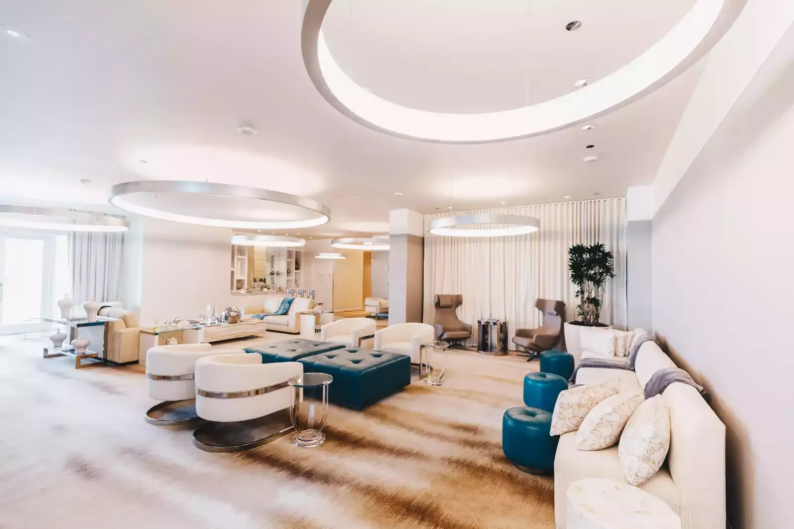 A room at ESPA with white sofas and armchairs, teal pouffes, pale curtains and large ring lights on the ceiling.