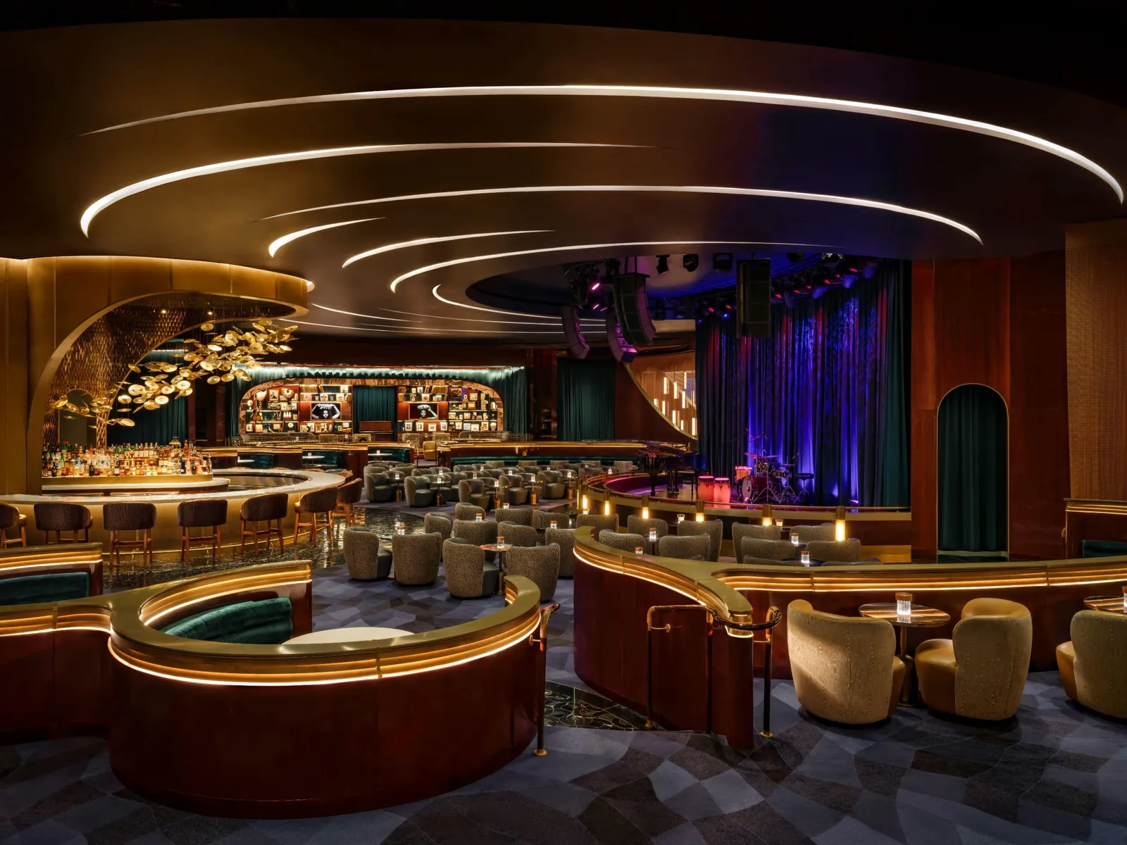 Jon Batiste’s Jazz Club: curved booths with ochre armchairs, the lit bar on the left and, at the back, the stage with its blue curtain.