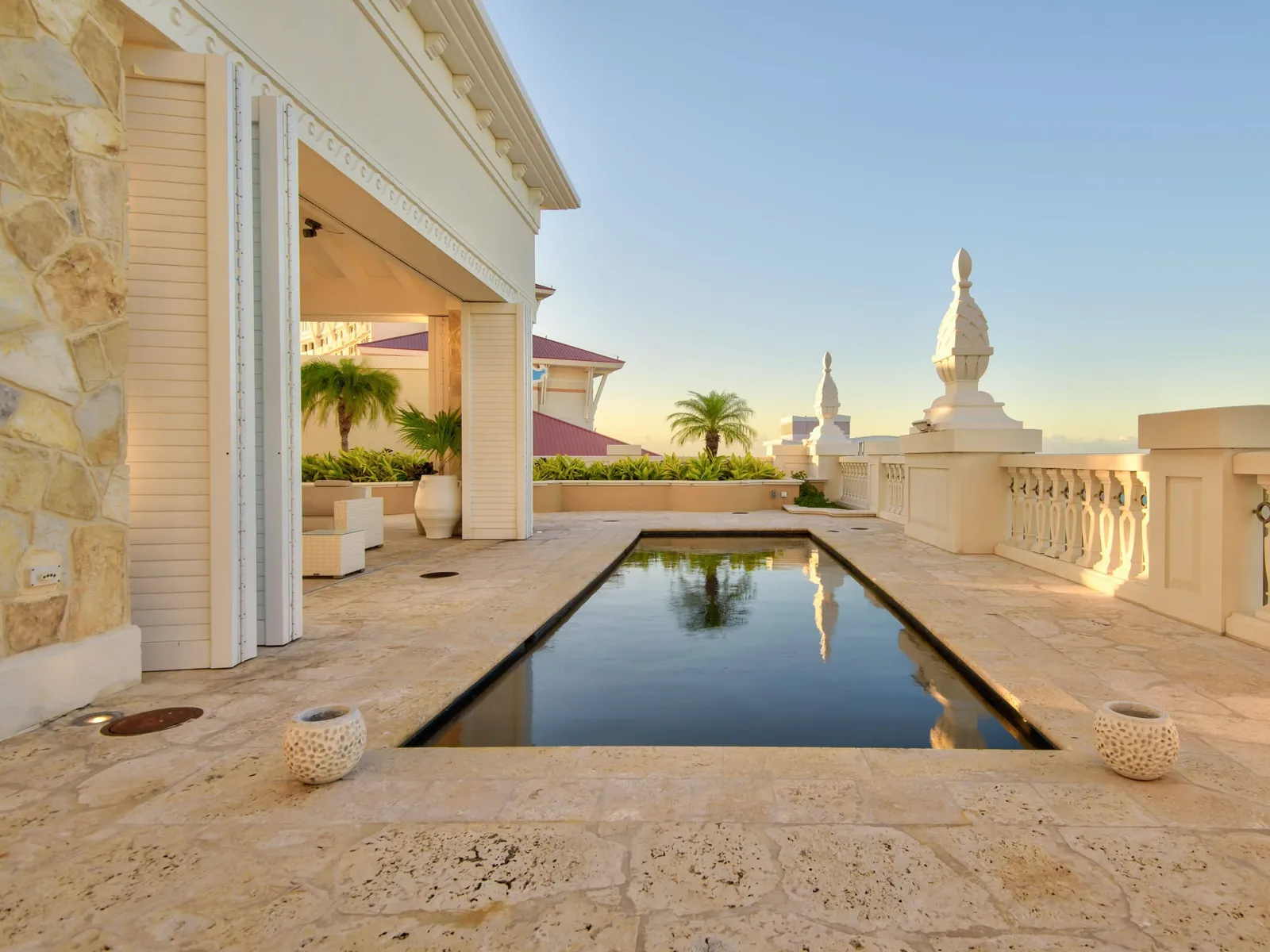 The Chairman Suite’s terrace at sunset: a narrow dark pool in the pale stone floor, the white balustrade and the resort’s pink roofs.