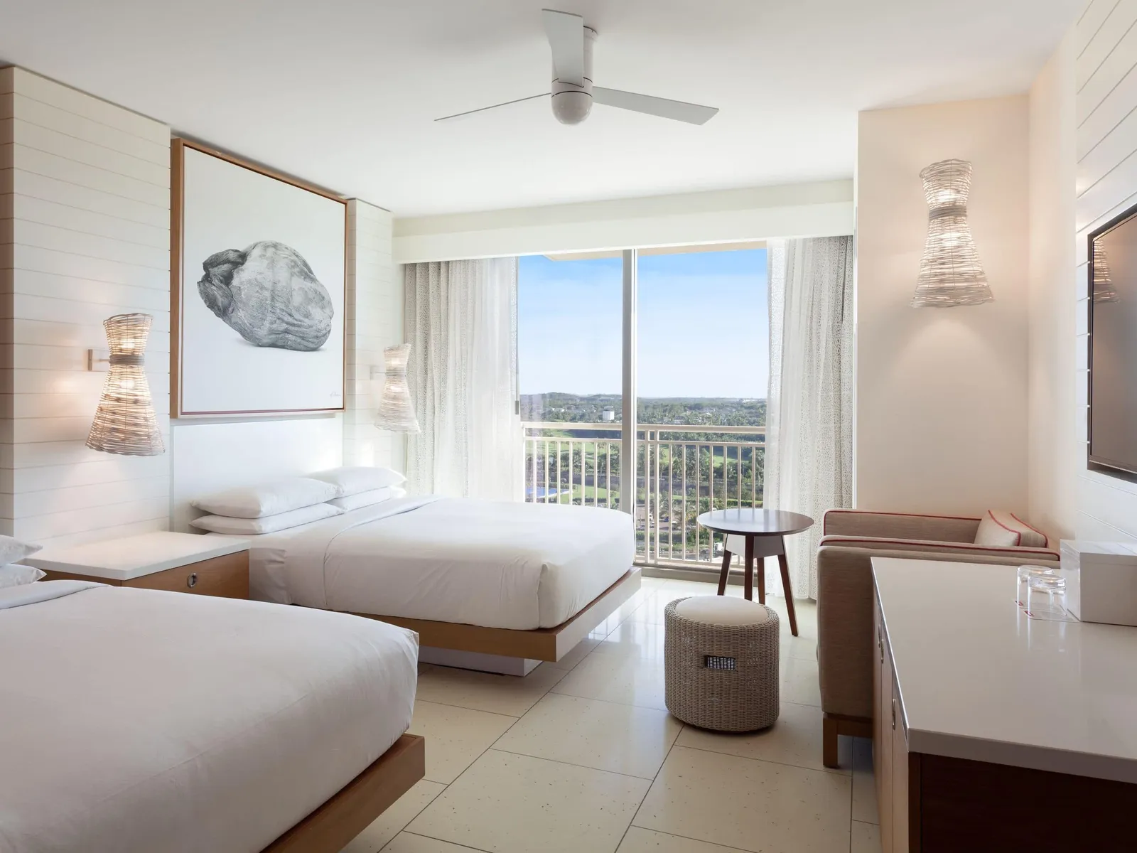 One of the 2 connecting rooms: 2 queen beds, a small round wooden table, a wicker stool and the glass door over the golf course.