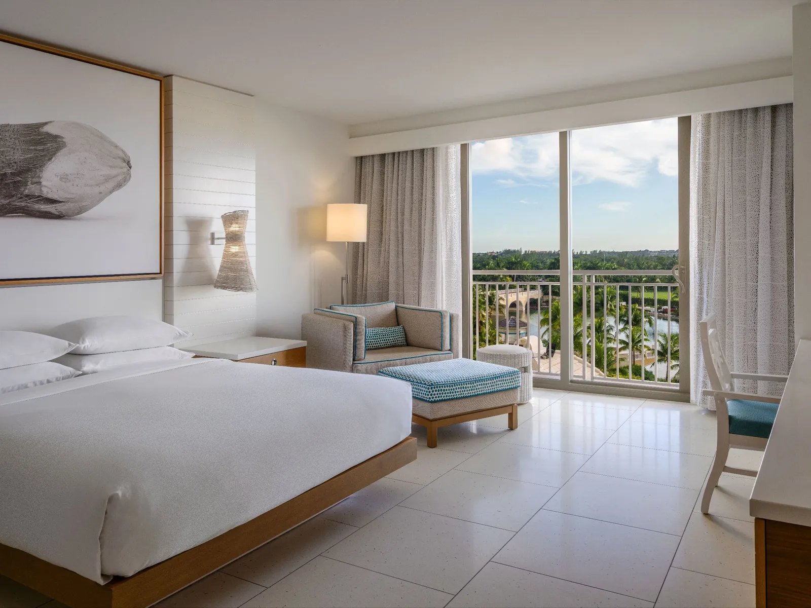 A king room with fountain view: the white bed, the armchair with its pale-blue footstool and the glass door over the gardens and the fountain lake.