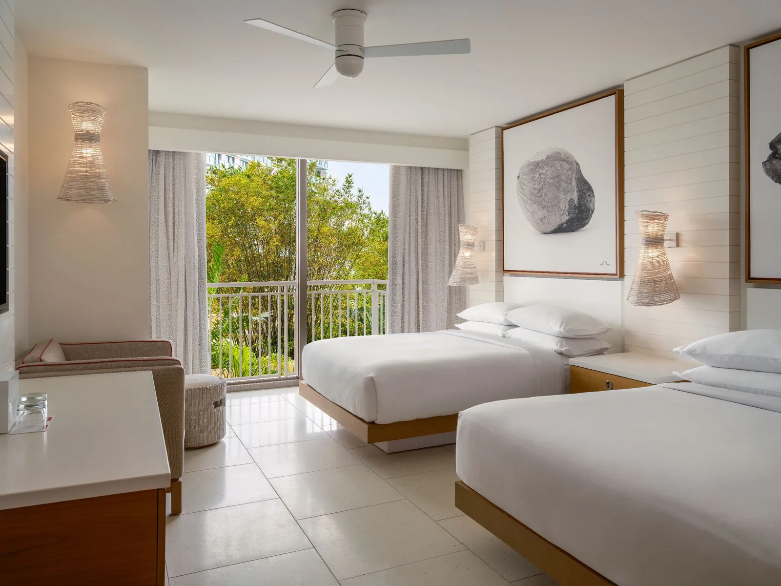 A room with 2 queen beds in the West Tower, with a ceiling fan, wicker wall lights and the railed glass door over the trees.