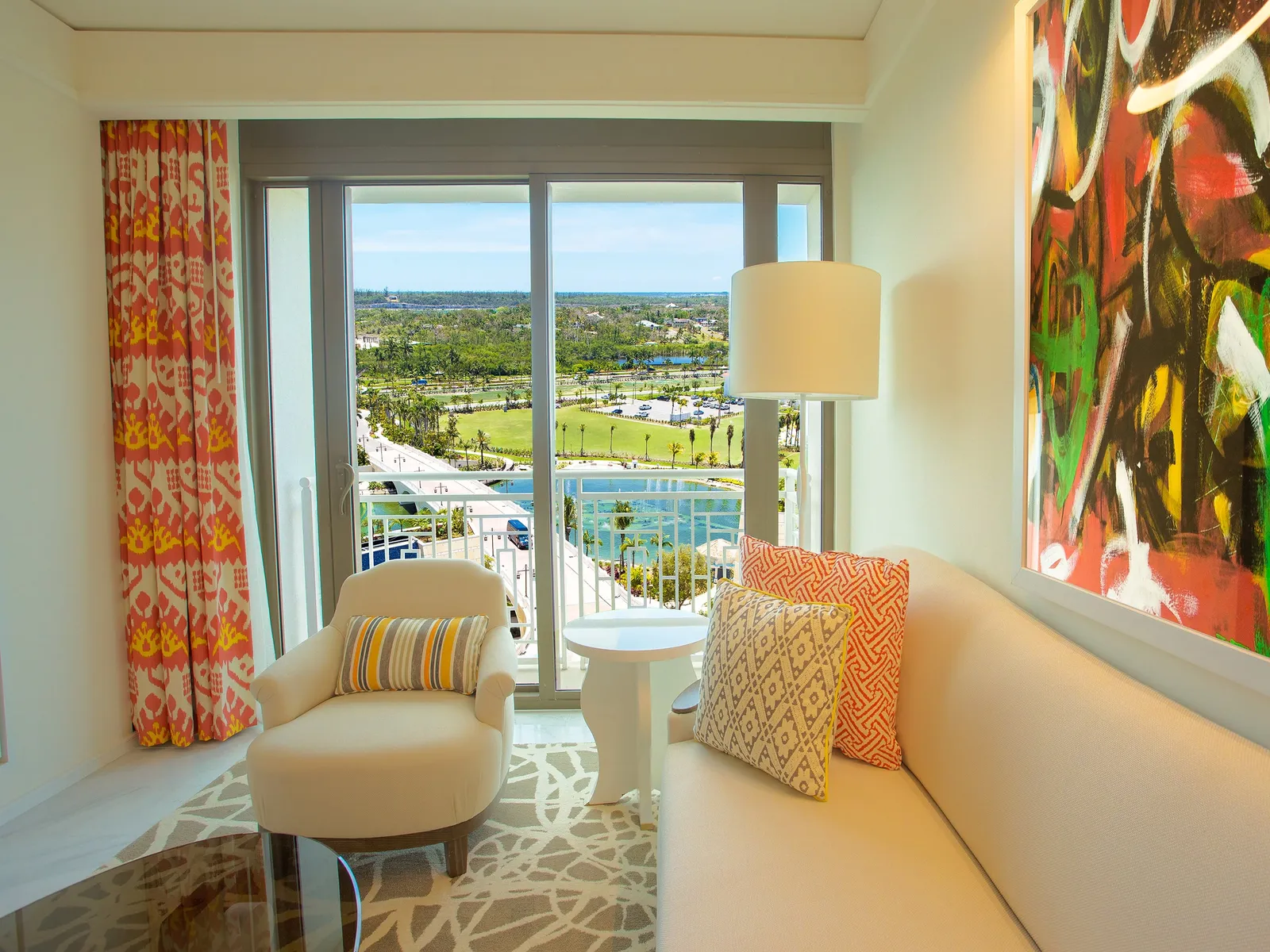 The sitting room of a Reserve residence: a pale sofa with orange cushions, an armchair, red curtains and the window over the fountain lake and the golf course.