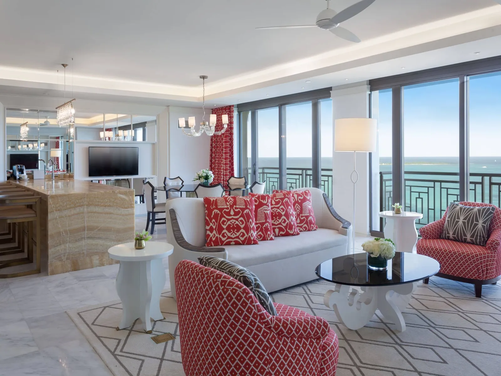 The Riviera residence’s living room: sofas and armchairs with red-patterned cushions, a round black table, the onyx bar and the windows over the sea.