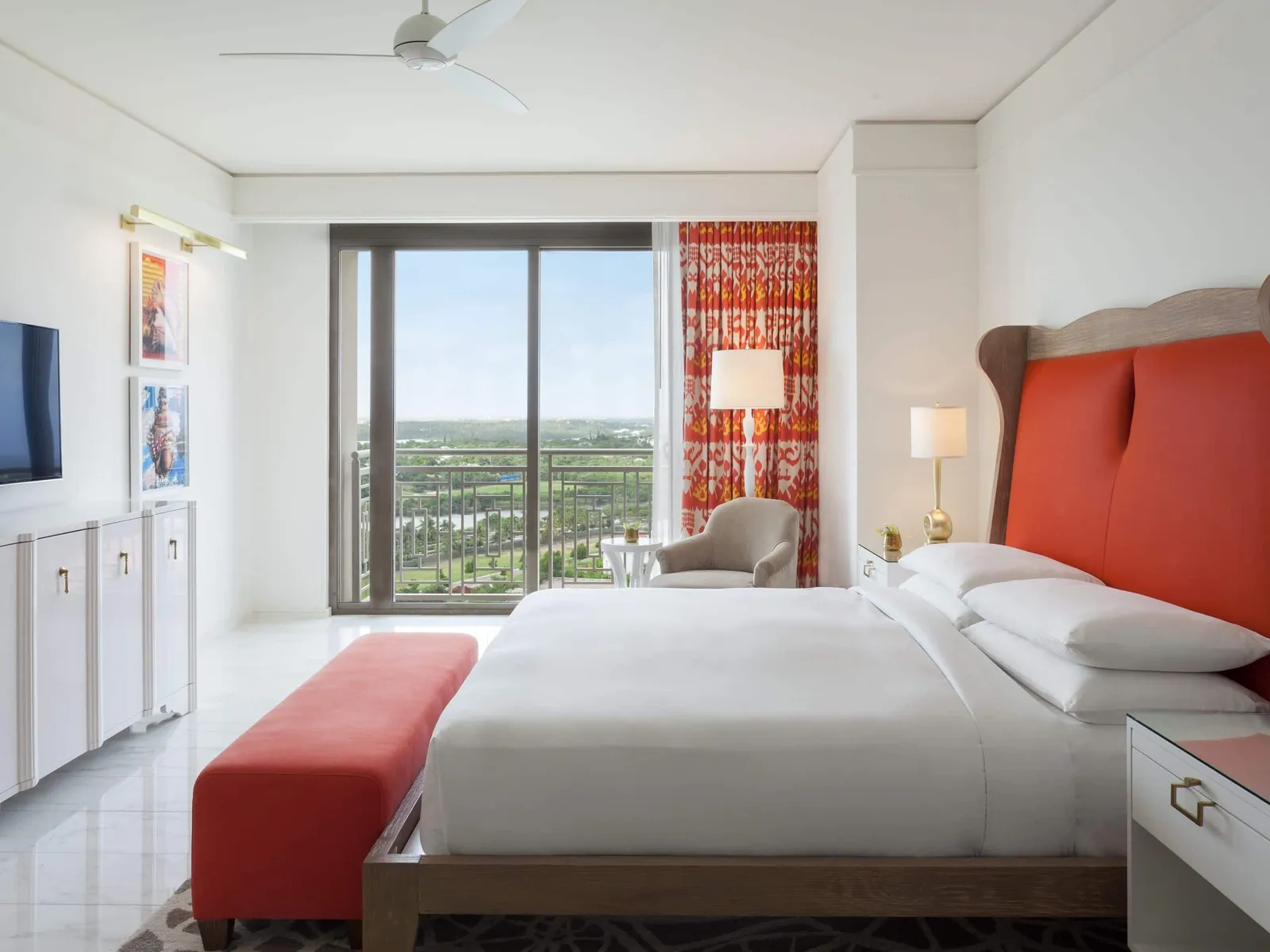 A bedroom of the Reserve 2-bedroom residence: the bed with its red headboard, the grey armchair and the glass door over the island’s greenery.