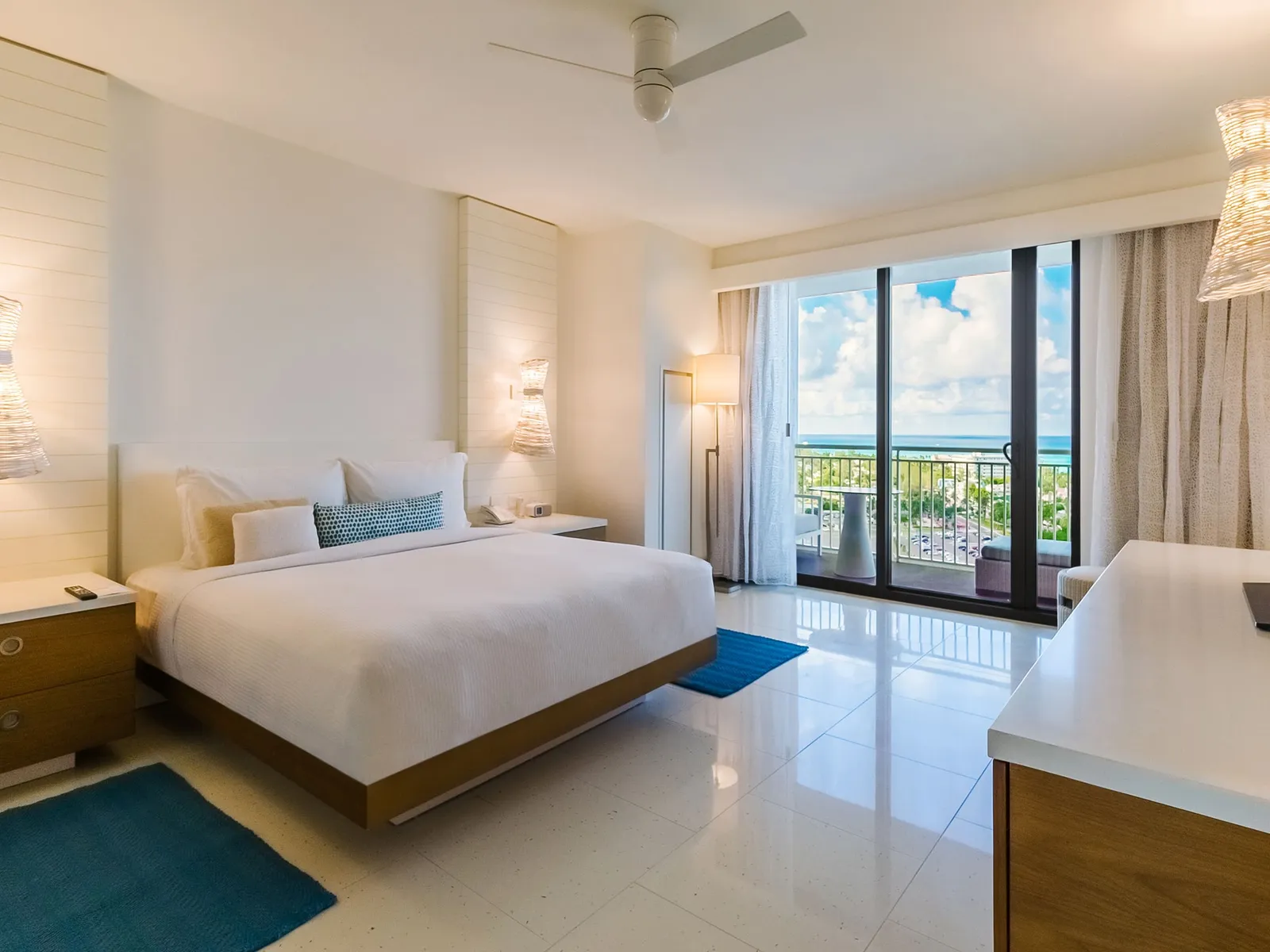 A bedroom of the 3-bedroom residence: the king bed with pale-blue cushions and the dark-framed glass door open onto the balcony and the beach.