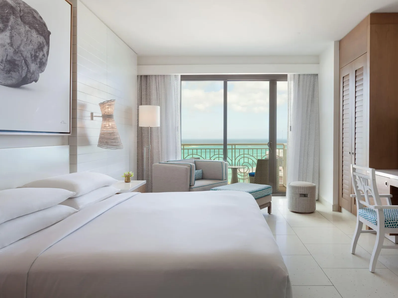 A bedroom of the 2-bedroom residence in the West Tower: the king bed, the wardrobe’s wooden louvres and the glass door to the balcony and the sea.