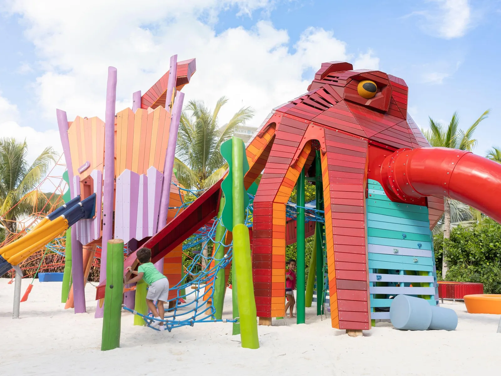 The Sandy Cay playground: a large red wooden octopus with a slide, colourful climbing frames and a child on the sand.
