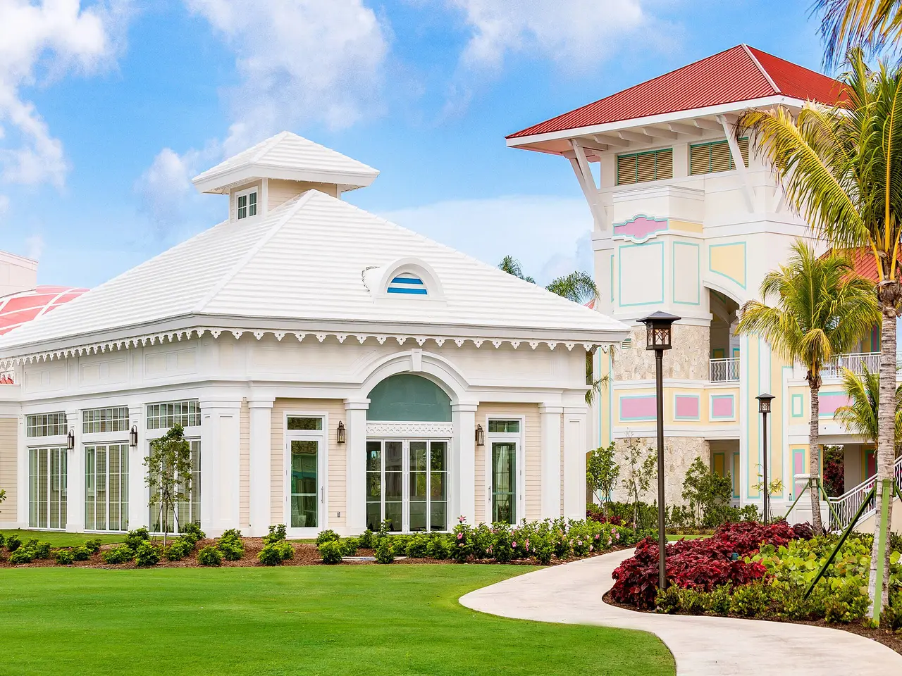 The white chapel with its hipped roof and lantern, among lawn, red flower beds and palms.