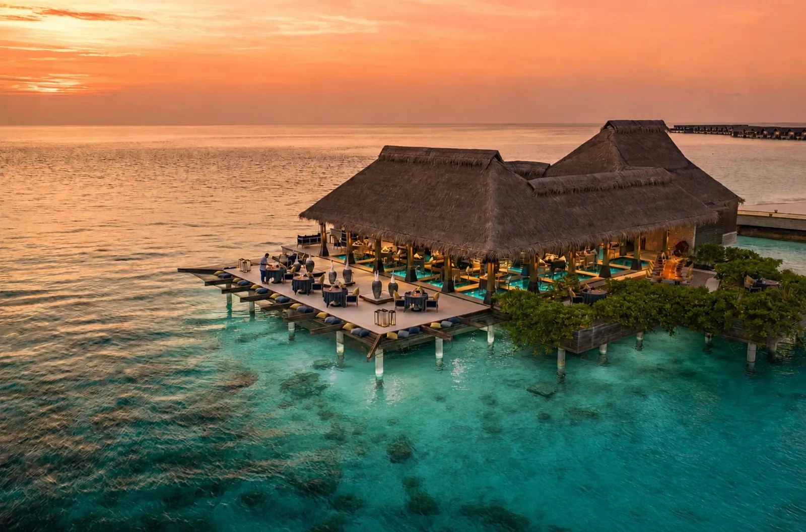 FireDoor from above at sunset: the thatched pavilion over the water, its outdoor tables above the reef.