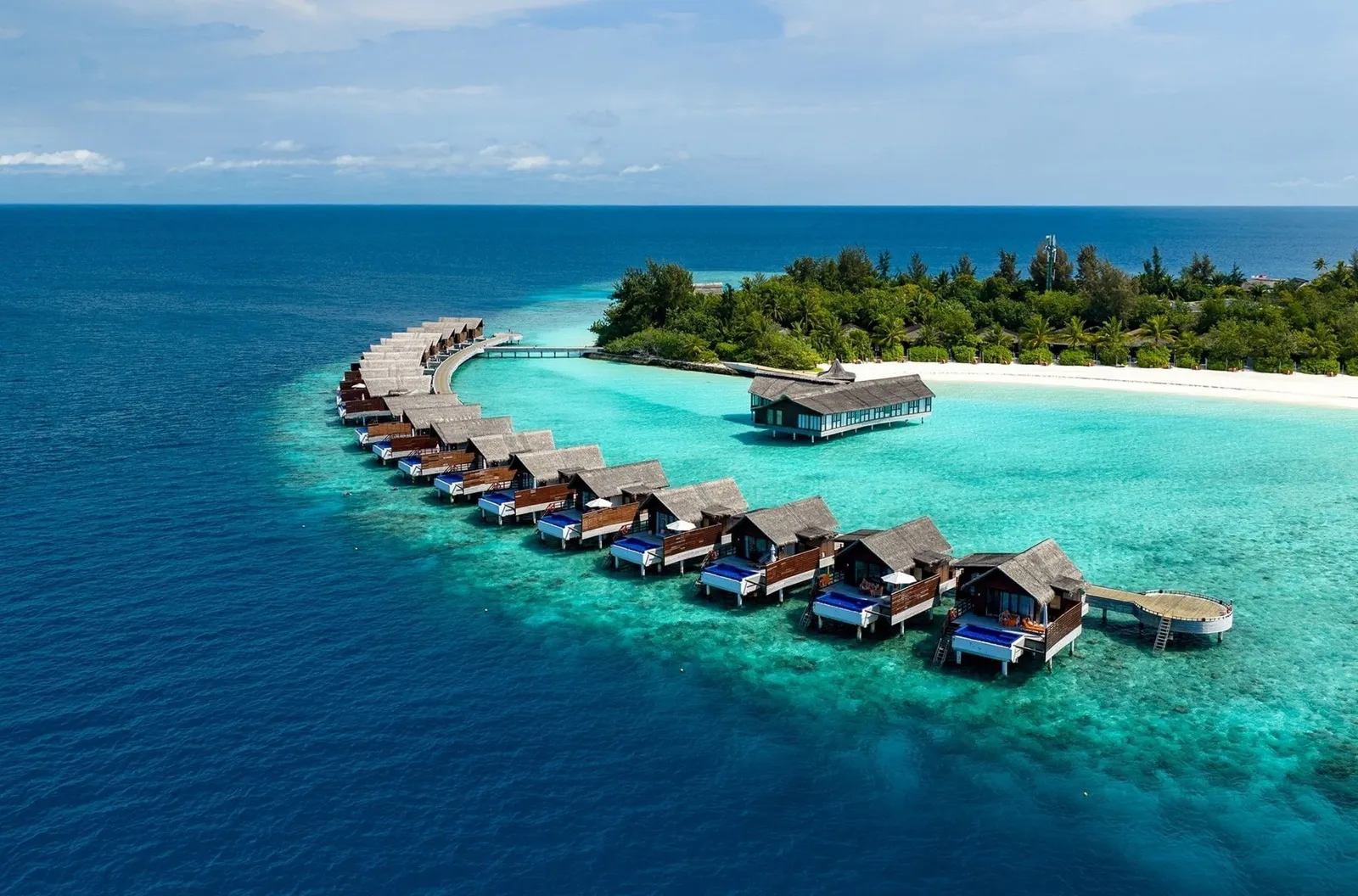 The curving row of thatched water villas above the reef, with the island, its beach and the overwater restaurant behind.