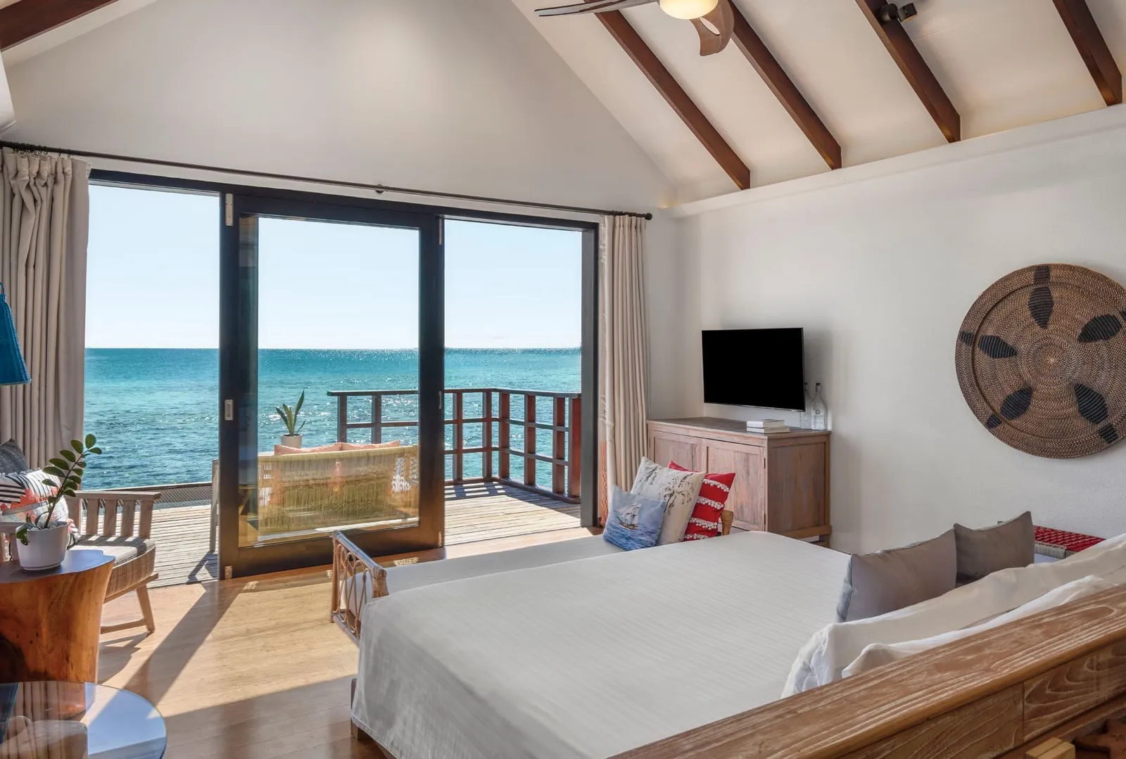 A Lagoon Water Villa bedroom: the bed, the sofa and the glass door open onto the deck and the lagoon.