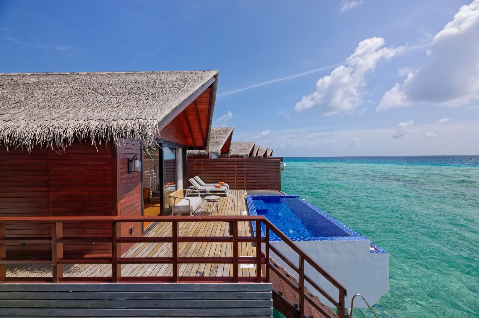 The deck of a Pool Water Villa over the water, with its private pool, the loungers and the turquoise lagoon.