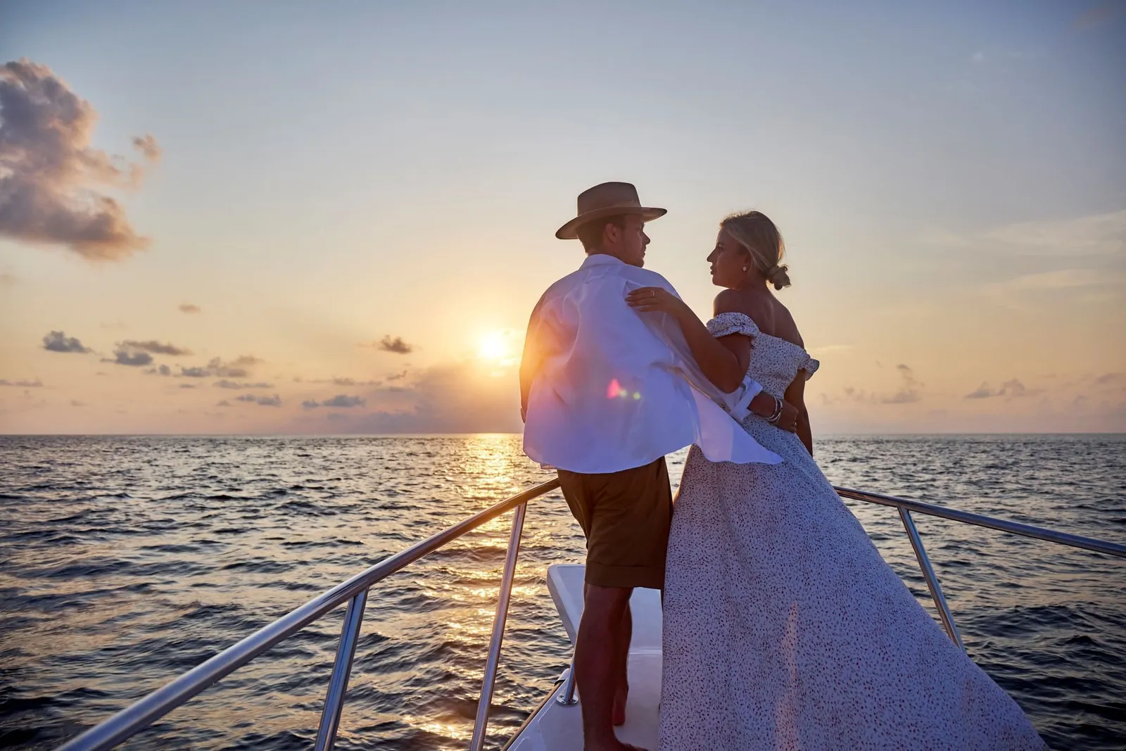 A couple embracing at the bow of a boat at sunset, above the sea.