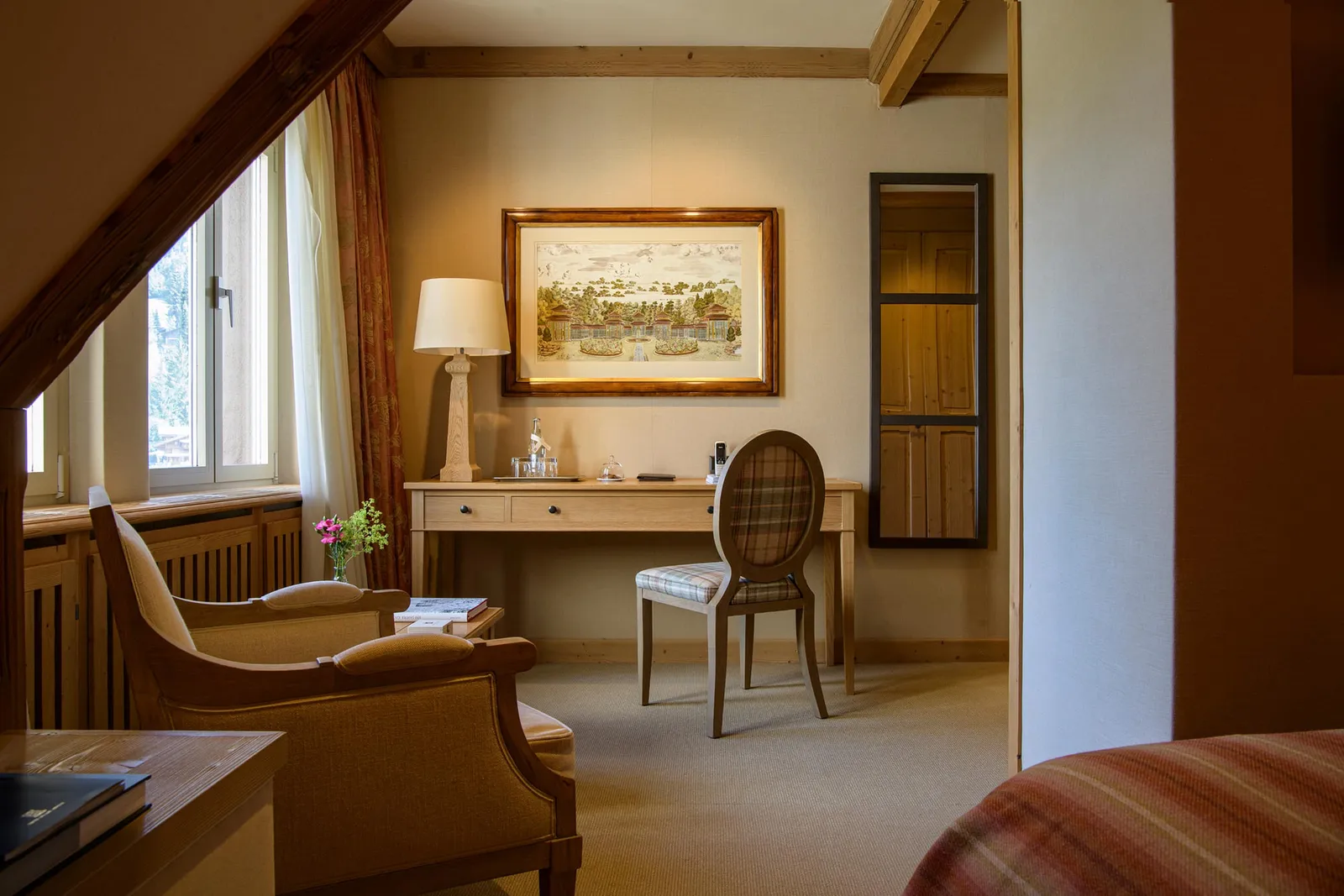 A Cosy Room under the sloping roof: an armchair, a writing desk with an oval-backed chair, a framed picture and the corner of the bed
