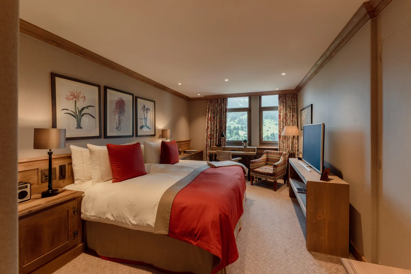 A Cosy Room Mountain View: a double bed with a red throw and cushions, botanical prints, a TV and an armchair by the window