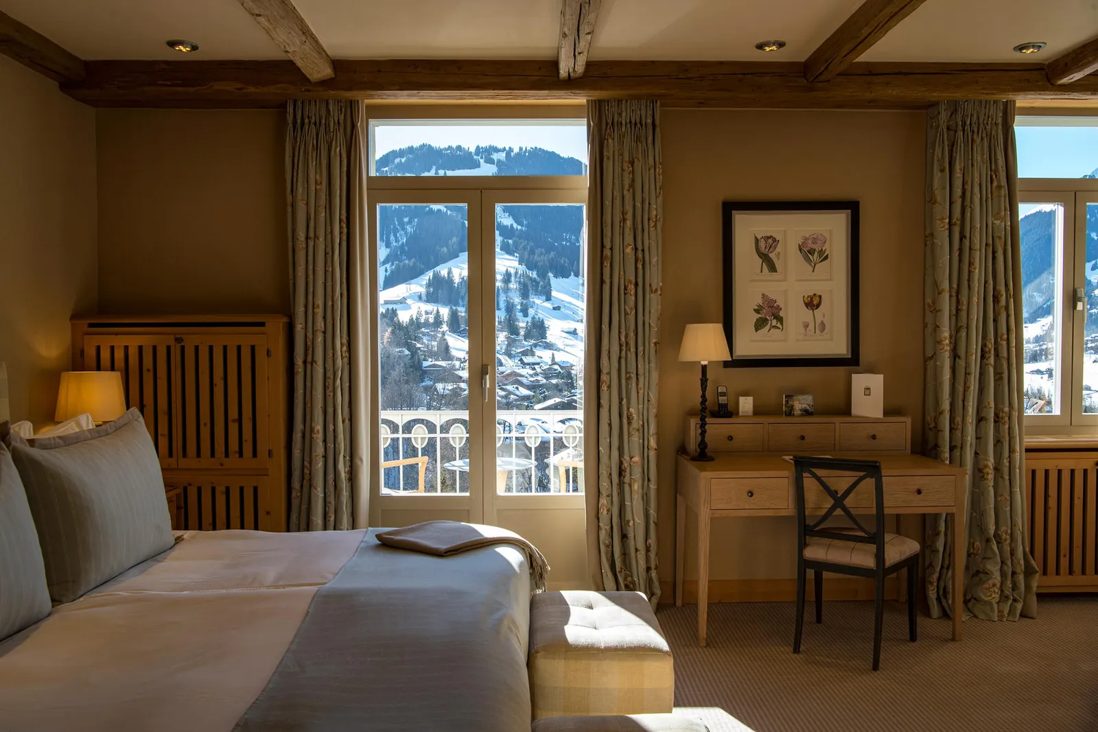 A Deluxe Room Mountain View: the bed facing French windows onto the balcony, with snowy slopes and chalets outside