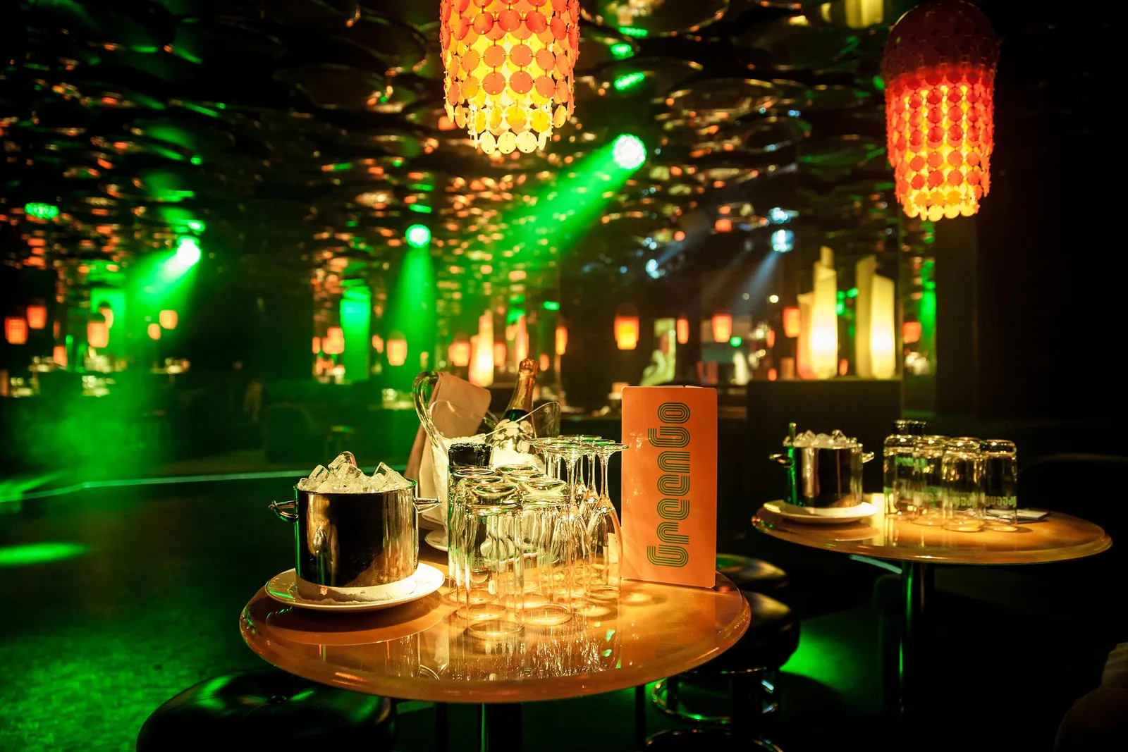 The GreenGo club: round tables with ice buckets, glasses and the club’s menu under green light beams and amber lanterns