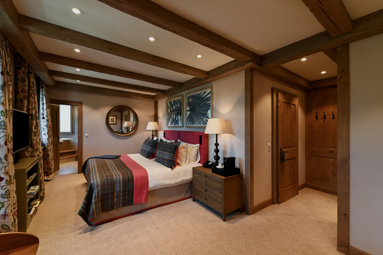 A Tower Junior Suite Mountain View: dark ceiling beams, a bed with a tartan throw and a red headboard, a round mirror and patterned curtains