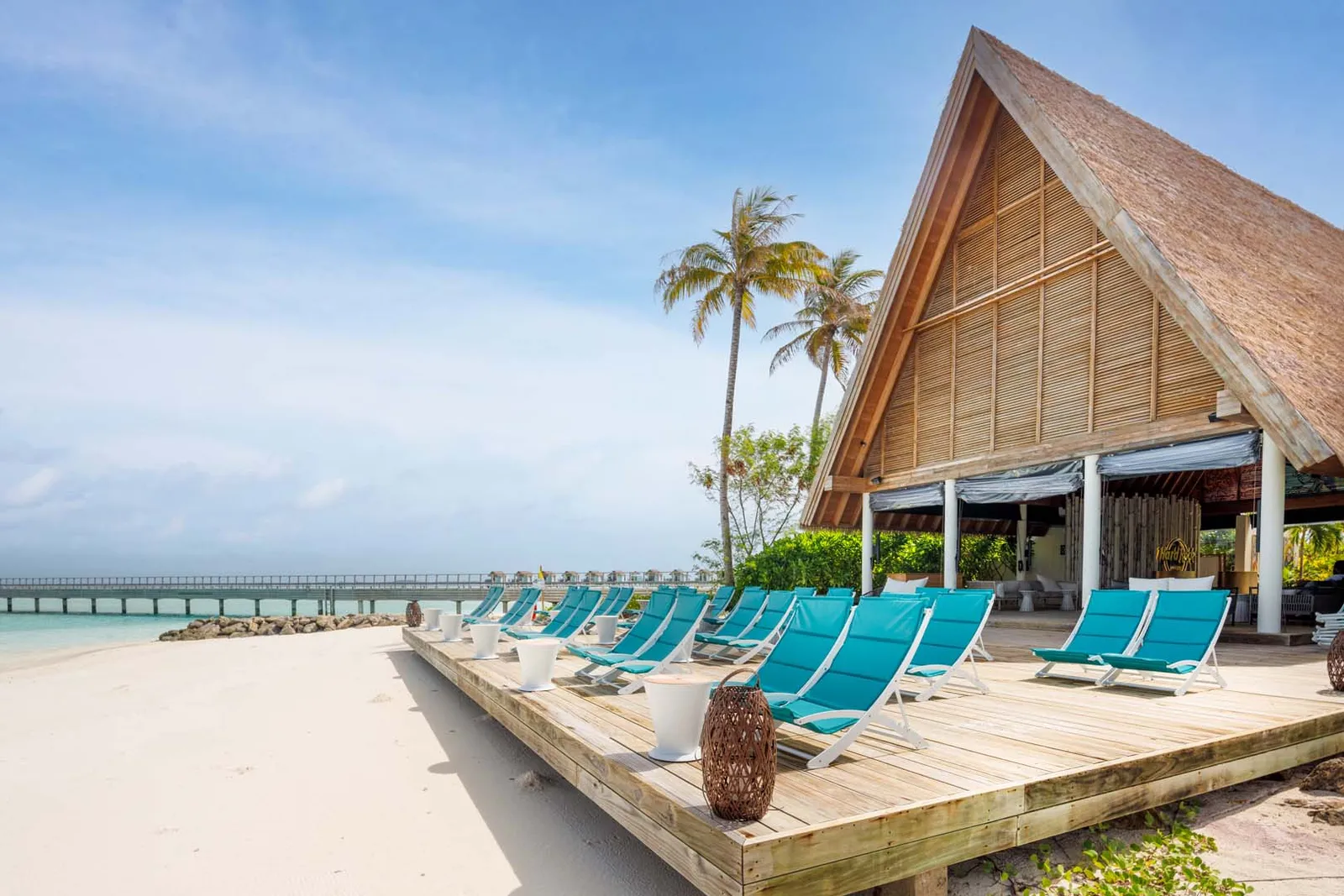The A-frame pavilion, turquoise loungers on its wooden deck and the jetty behind