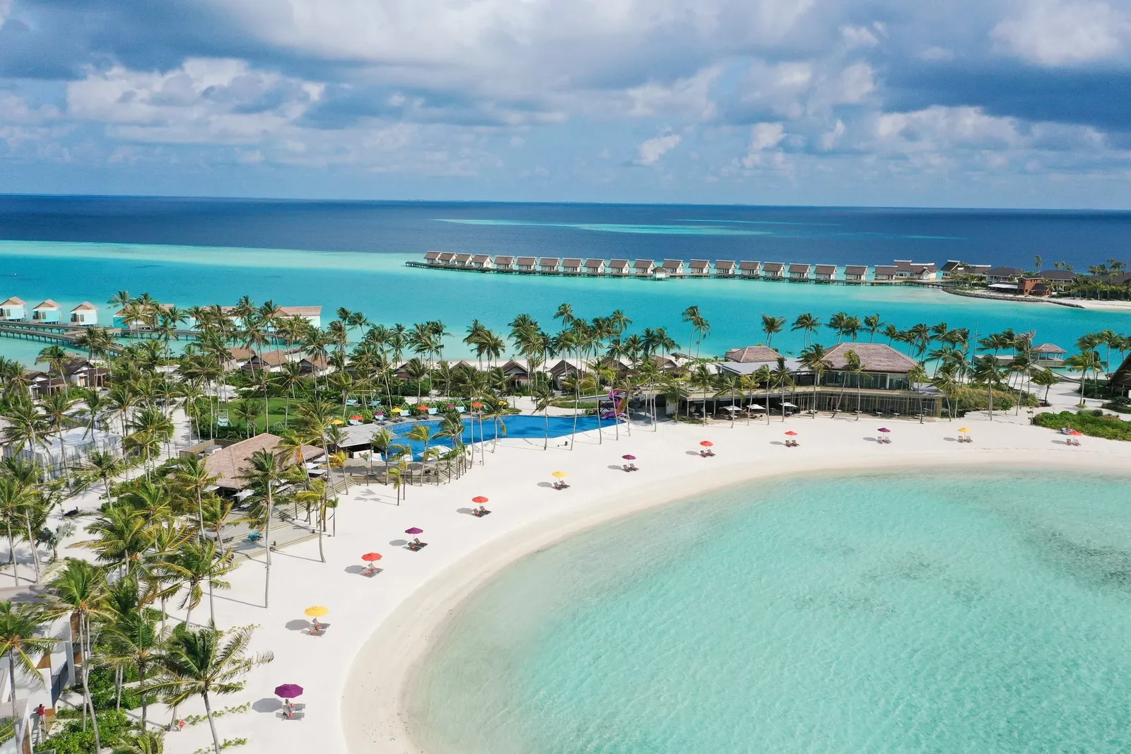 The crescent main beach from the air, coloured parasols and the shallow lagoon