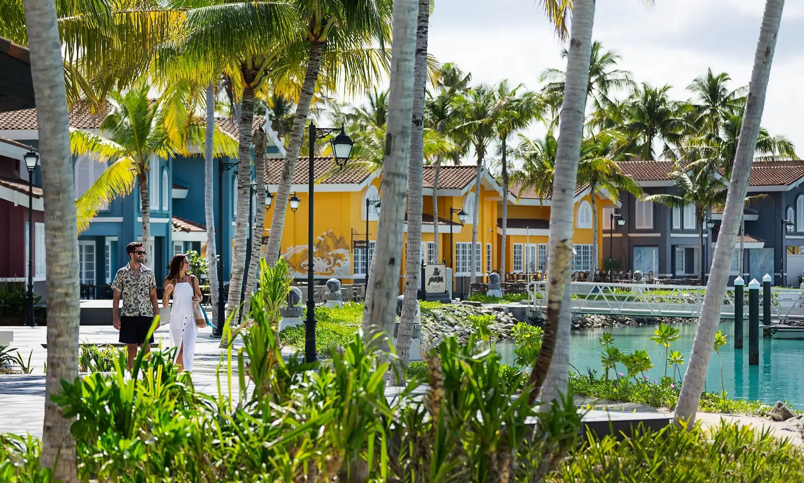 The Marina @ CROSSROADS: a couple walking under the palms past the coloured houses on the harbour