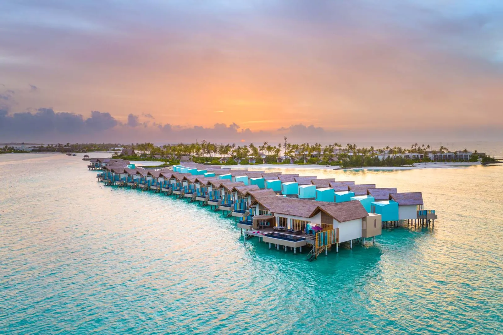 The overwater villas at sunset, a pink sky over the calm lagoon