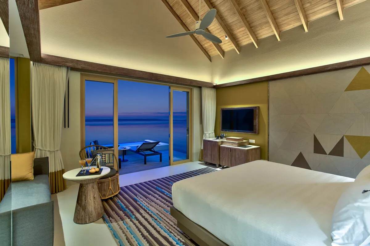 A Diamond Overwater Pool Villa bedroom at dusk, the deck and the blue sea beyond the glass