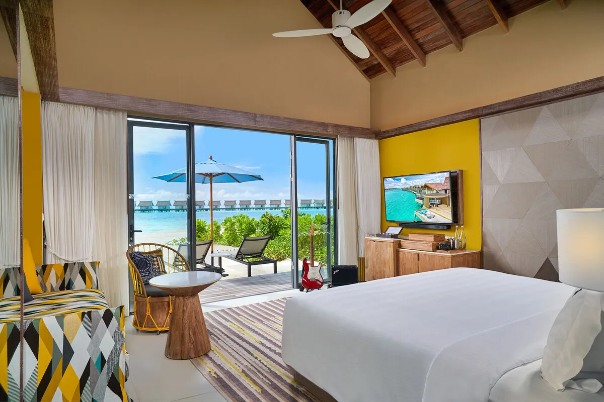 A Gold Beach Villa bedroom, its deck with loungers and the water villas in the distance