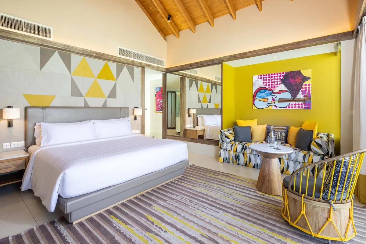 A Platinum Overwater Villa bedroom: the king bed, a yellow wall with a painted guitar and a diamond-patterned sofa