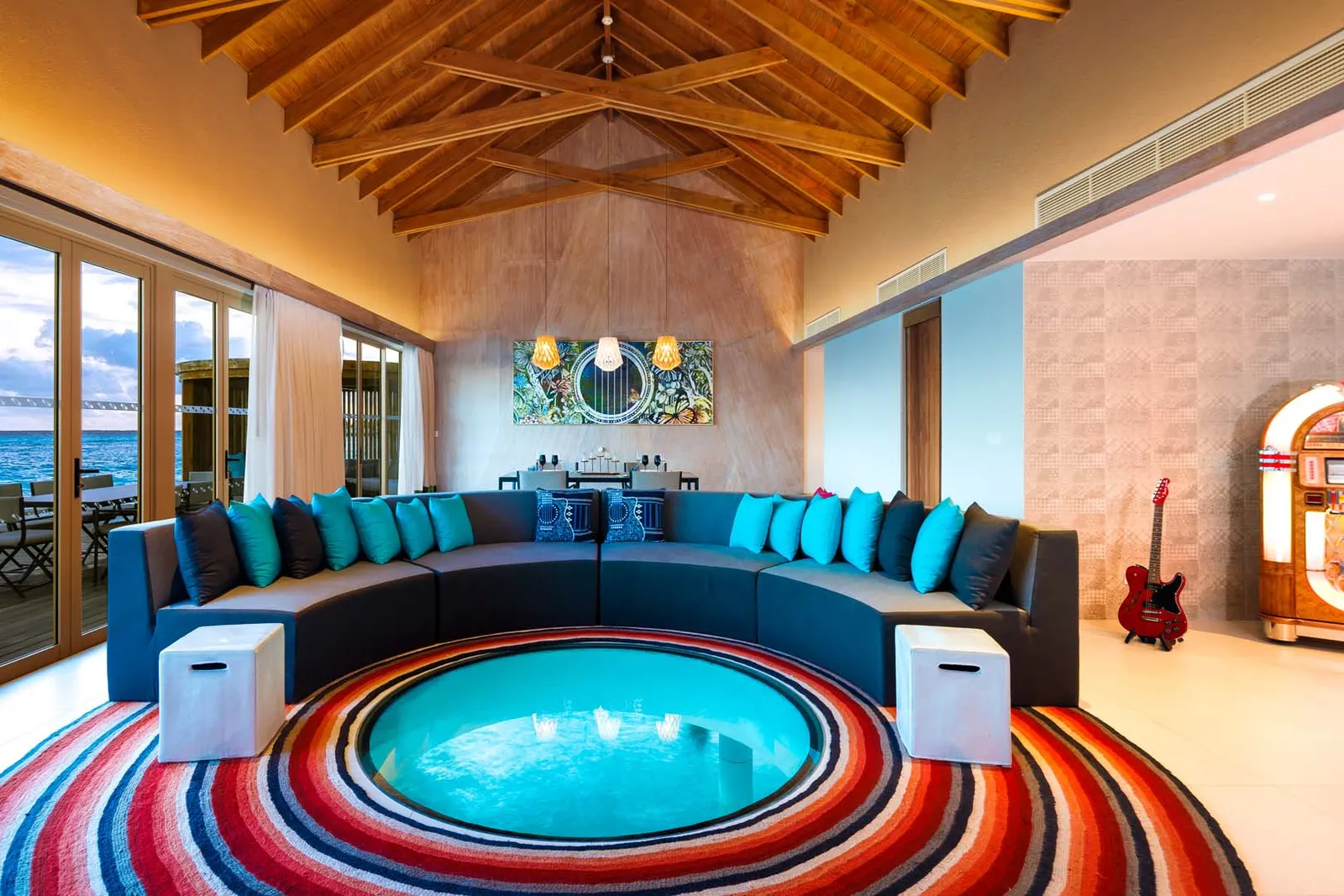 The Rock Star villa’s living room: a curved sofa round the glass floor panel, a jukebox and a red guitar