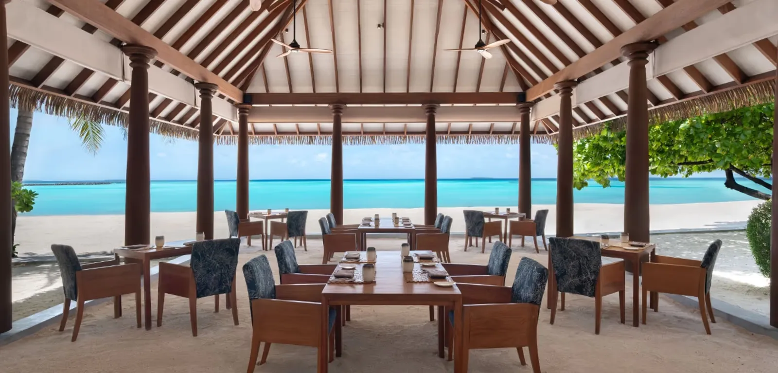 Tables and blue chairs beneath Ranba’s timber roof towards the lagoon