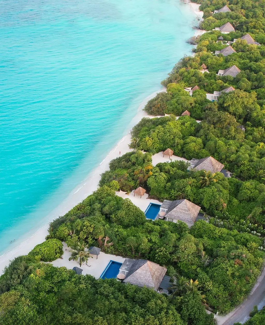 Aerial row of beach villas with long narrow blue pools between beach and villas.