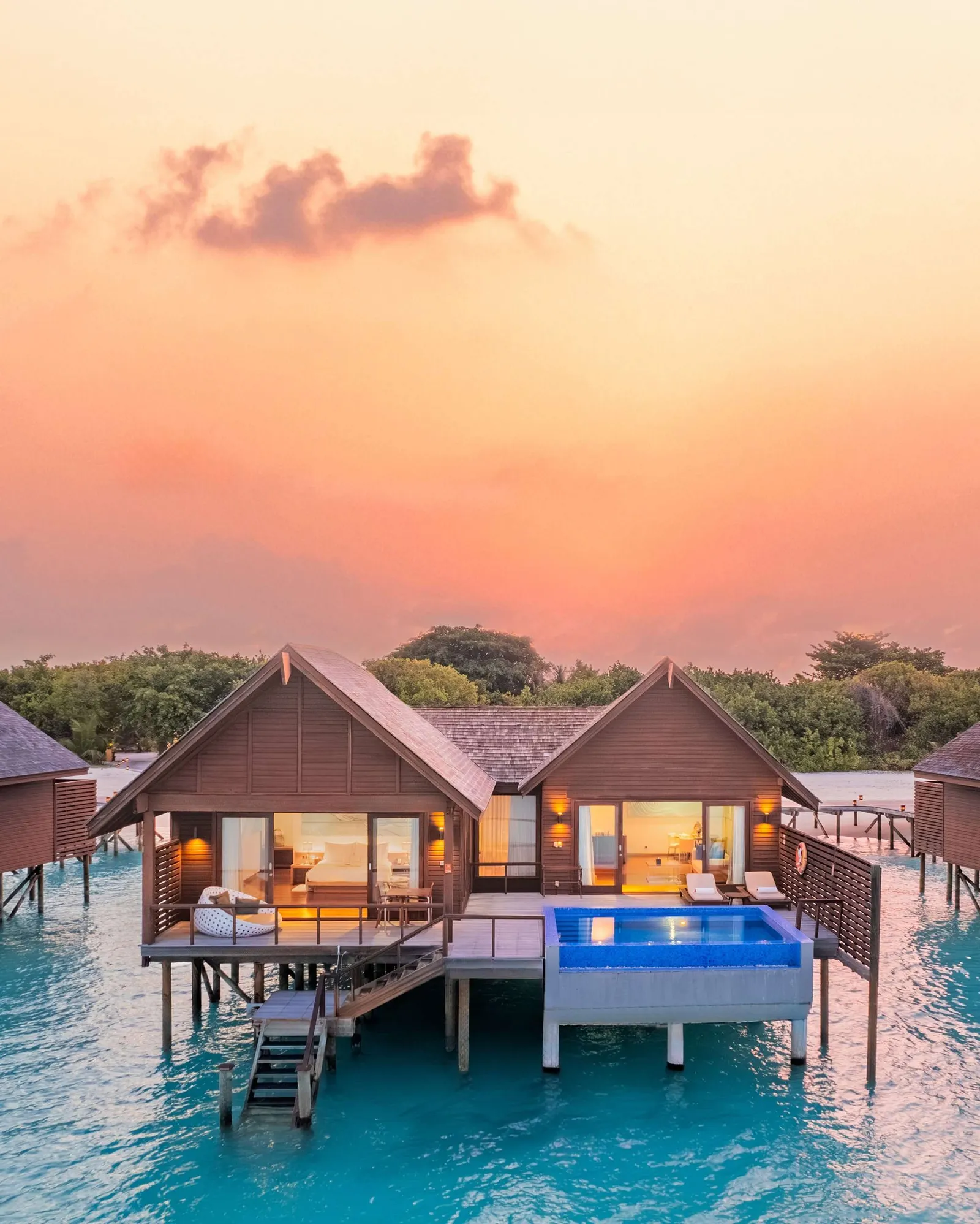 Sunset exterior water villa with 2 separate roof sections, furnished deck and rectangular pool.