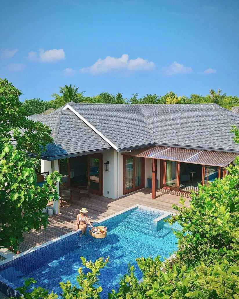 Beach villa pool with woman and floating breakfast tray, wooden deck, palms and doors.