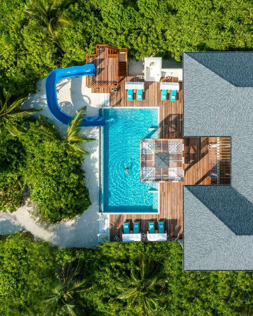 Vertical aerial large residence deck, central pool, blue waterslide and seating areas.
