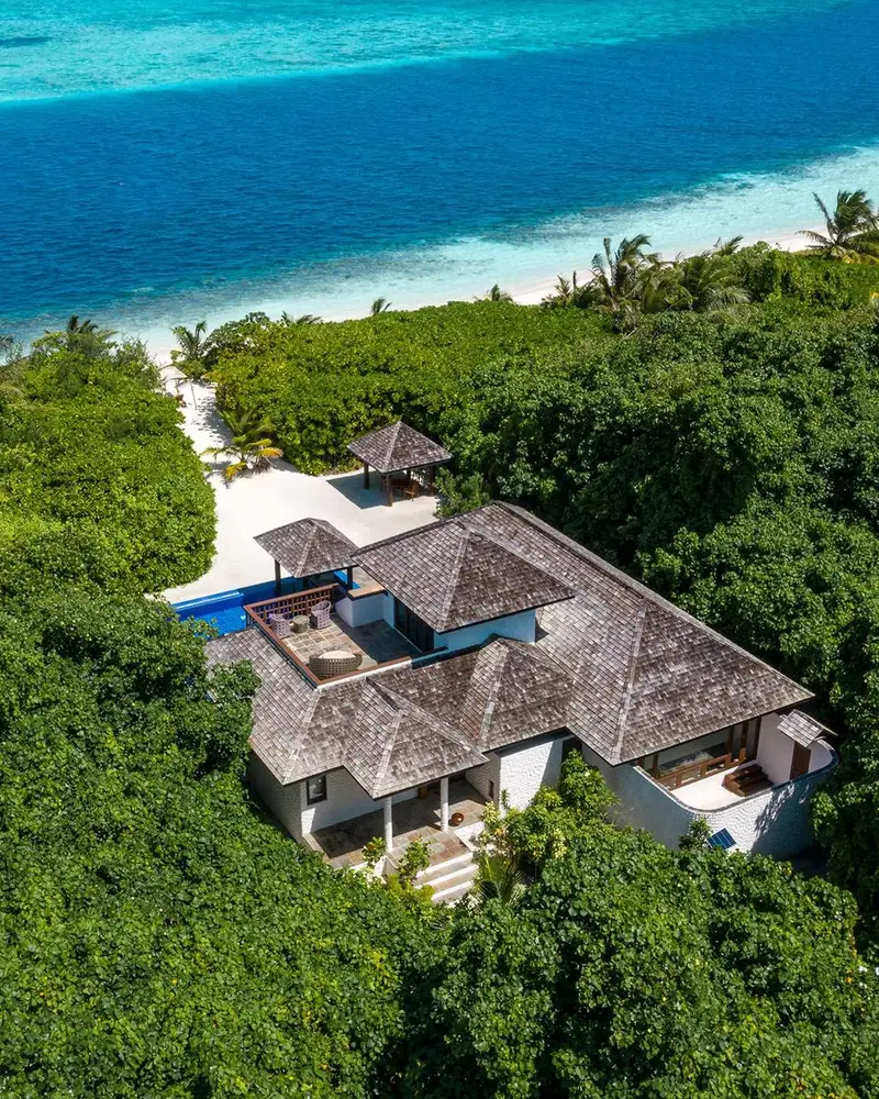 Aerial beach residence with multiple roof sections and pool amid dense vegetation.
