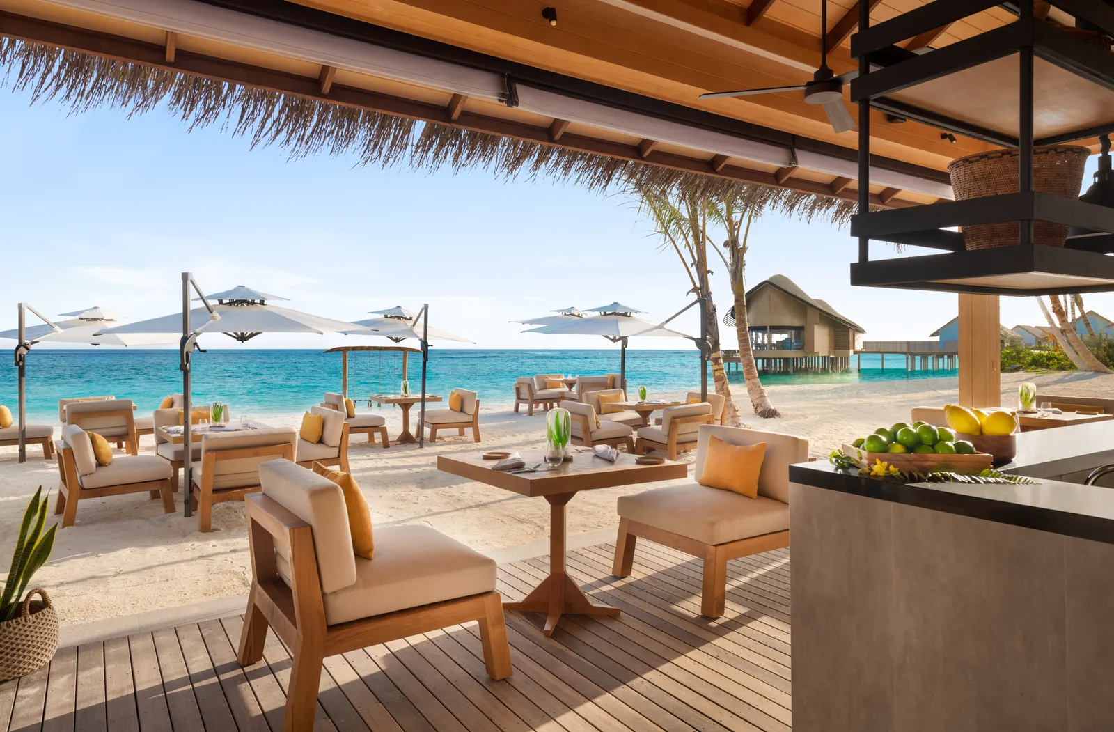 Beach Shack’s terrace on the sand, with parasols and the water villas beyond.