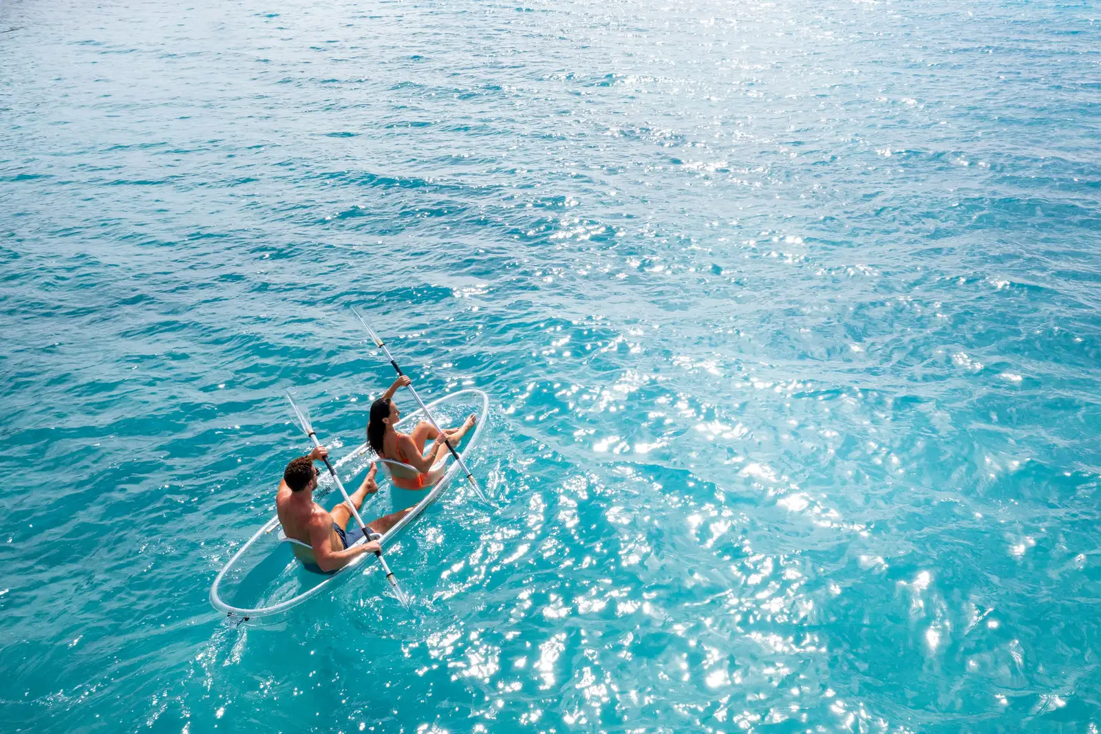 2 guests in a clear kayak on the lagoon, over bright water.