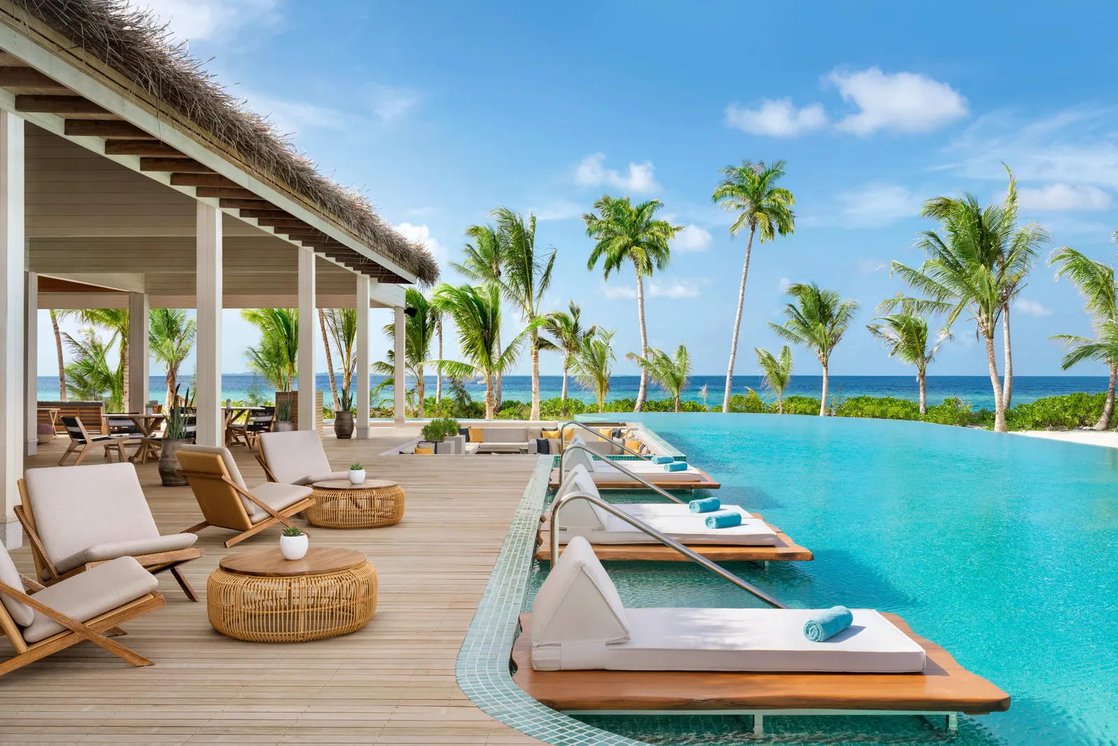 The main pool, loungers on its timber edge, palms and the sea on the horizon.