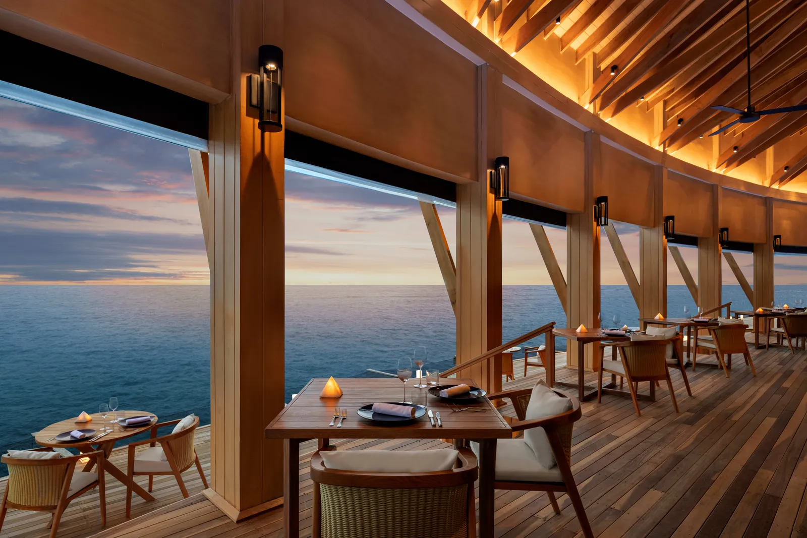 Origin’s overwater dining room at sunset: laid tables, candles and windows open to the ocean.