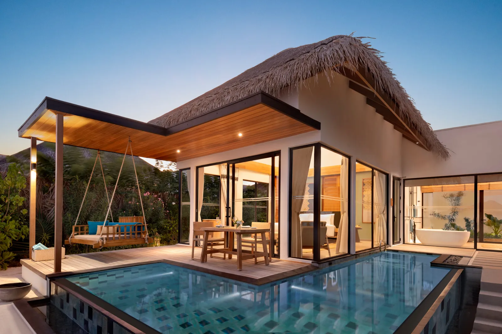 A One Bedroom Beach Pool Villa at dusk: the pool, the swing under the porch and the bedroom’s glass doors.