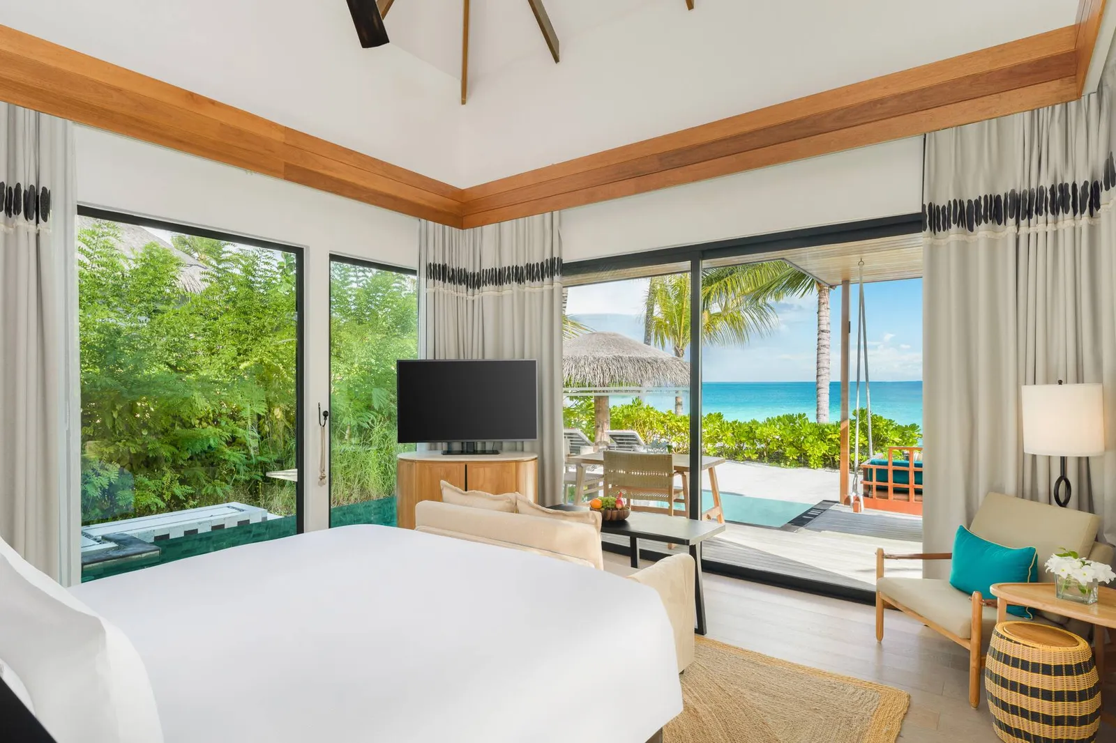 The bedroom of a One Bedroom Family Beach Pool Villa, with its sofa bed and windows on the garden and the sea.