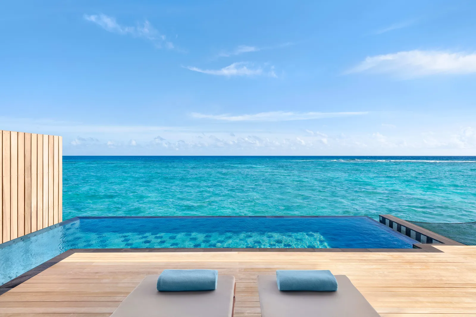 The deck of a One Bedroom Overwater Pool Villa: 2 loungers and the infinity pool over the ocean.