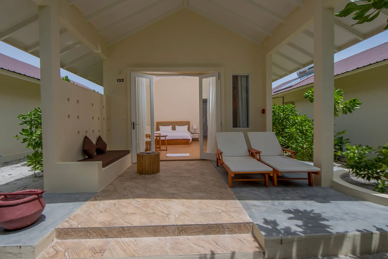 Il patio coperto di un Superior Beach Bungalow, con i 2 lettini, la panca e la porta aperta sulla camera.