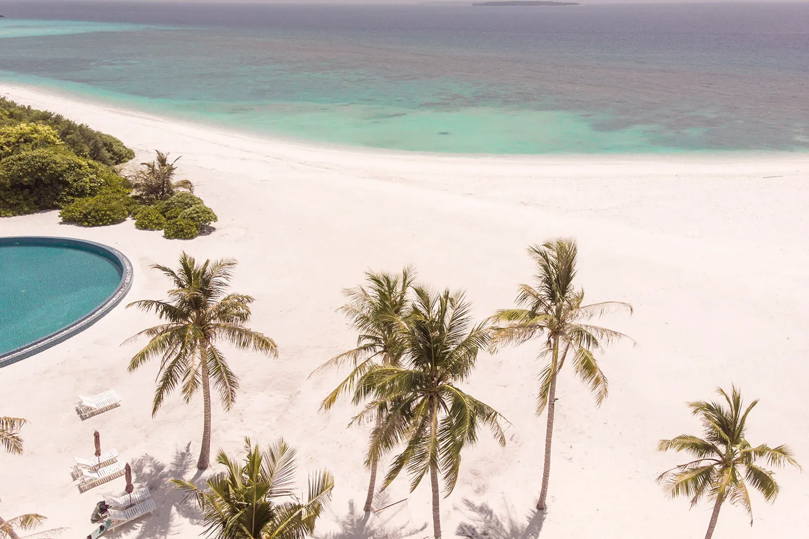 La spiaggia di Hondaafushi dall’alto: la sabbia bianca, le palme, il bordo della piscina e la laguna chiara.